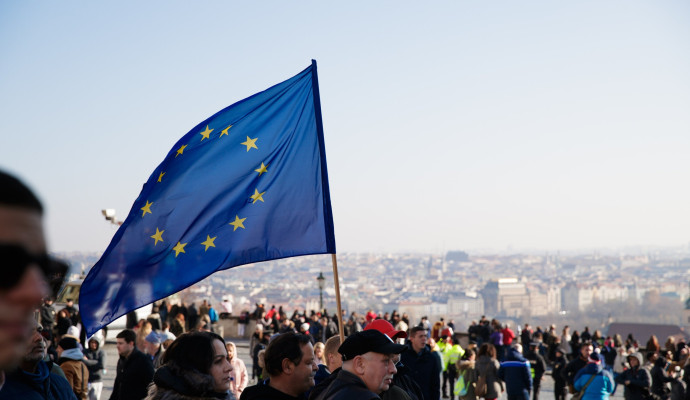 Bild einer Demonstration. Im Fokus steht eine EU Flagge, die im Wind weht